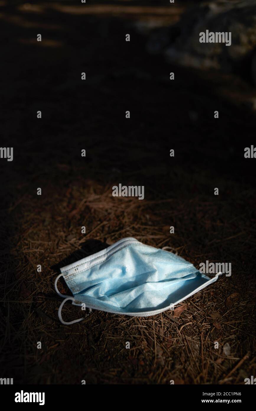 primo piano di una maschera chirurgica blu utilizzata gettata sul terreno nei boschi Foto Stock