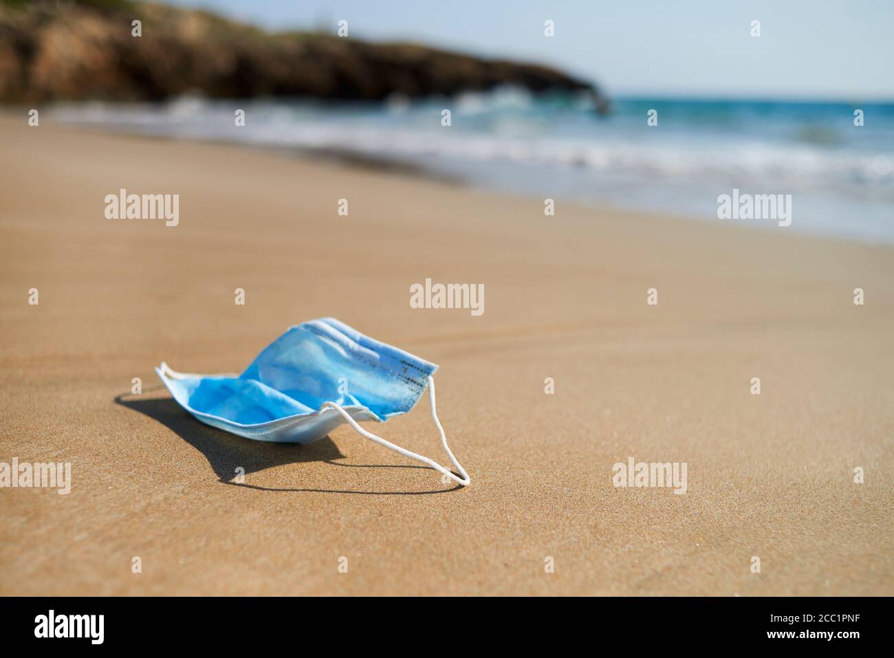 primo piano di una maschera chirurgica blu usata gettata, o riportata dall'oceano, sulla sabbia bagnata della riva di una spiaggia solitaria Foto Stock