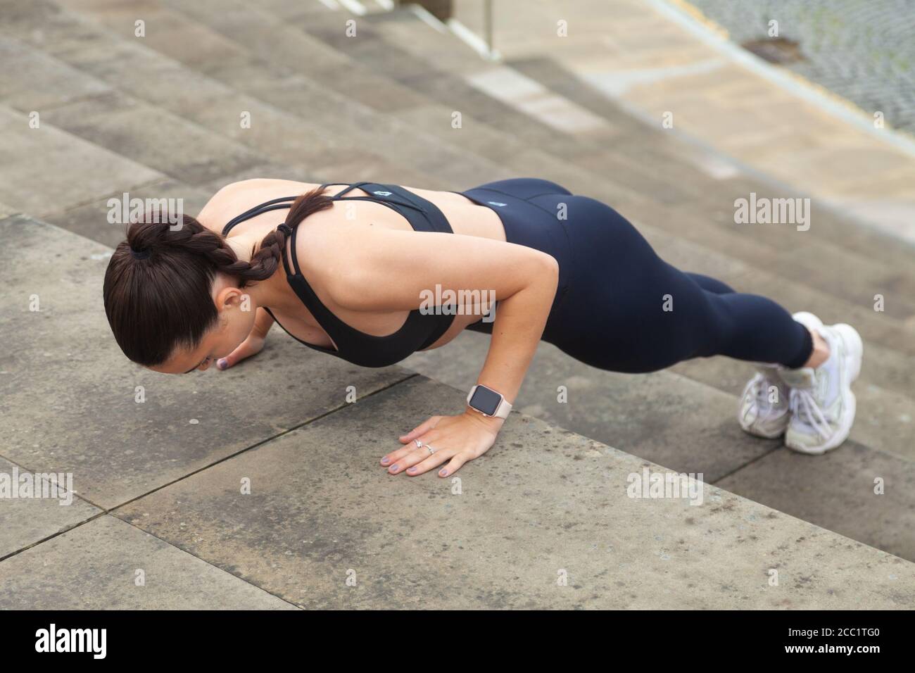 Indossa una giovane donna che indossa abbigliamento sportivo facendo una pressione sui gradini all'esterno Foto Stock