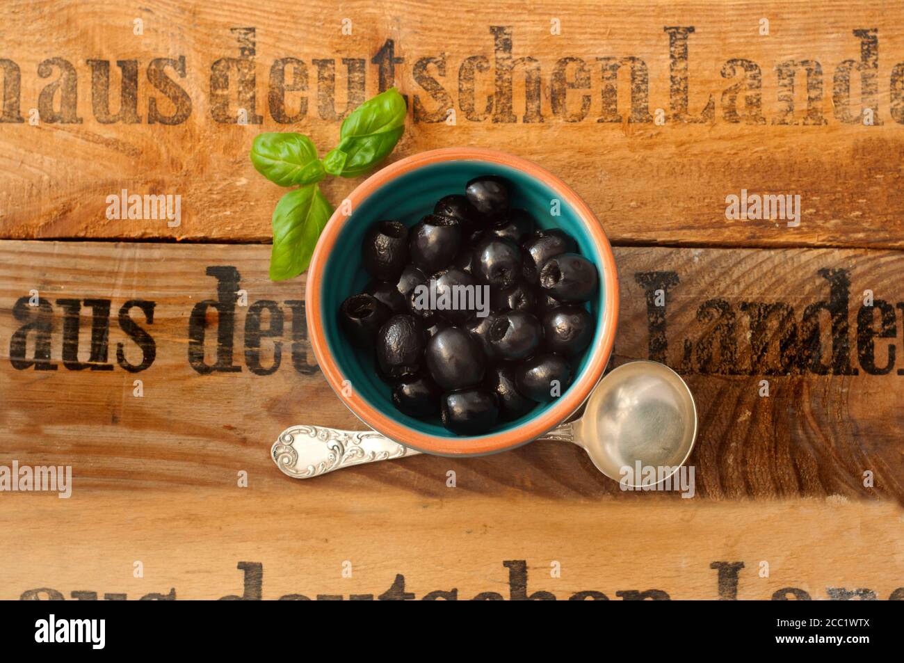 Ciotola di olive nere con il cucchiaio sul tavolo di legno, close up Foto Stock