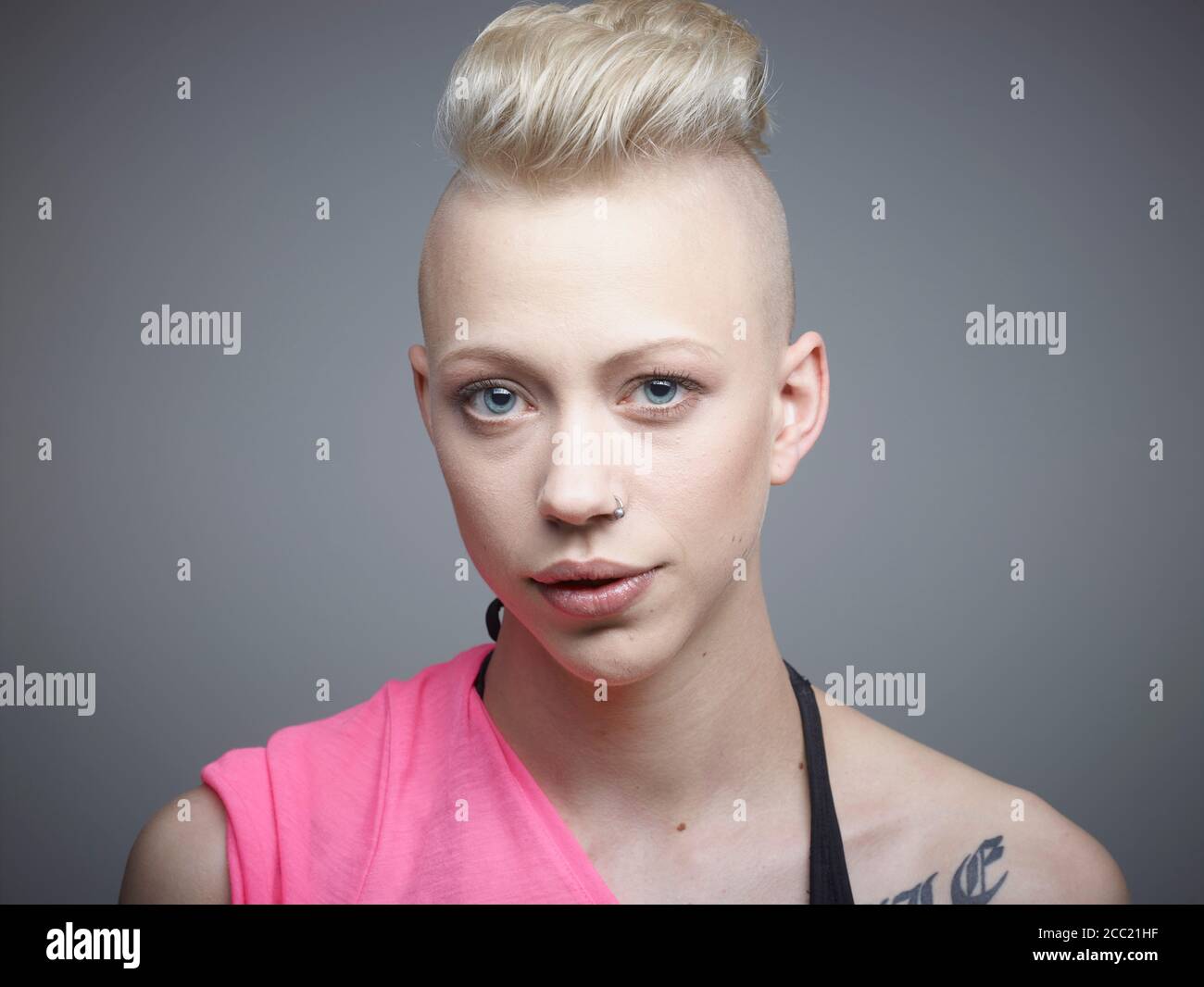 Ritratto di giovane donna con tatuaggi contro uno sfondo grigio, sorridente Foto Stock