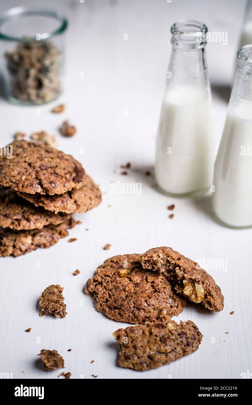 Bottiglie di latte con biscotti al cioccolato e un bicchiere di noci su tavola, close up Foto Stock