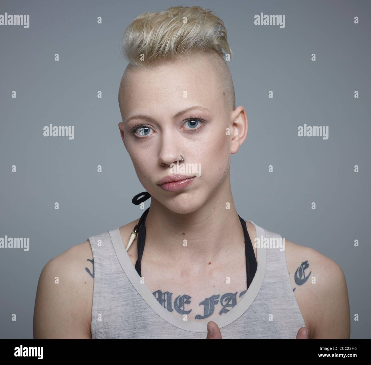 Ritratto di giovane donna con tatuaggi contro uno sfondo grigio, sorridente Foto Stock