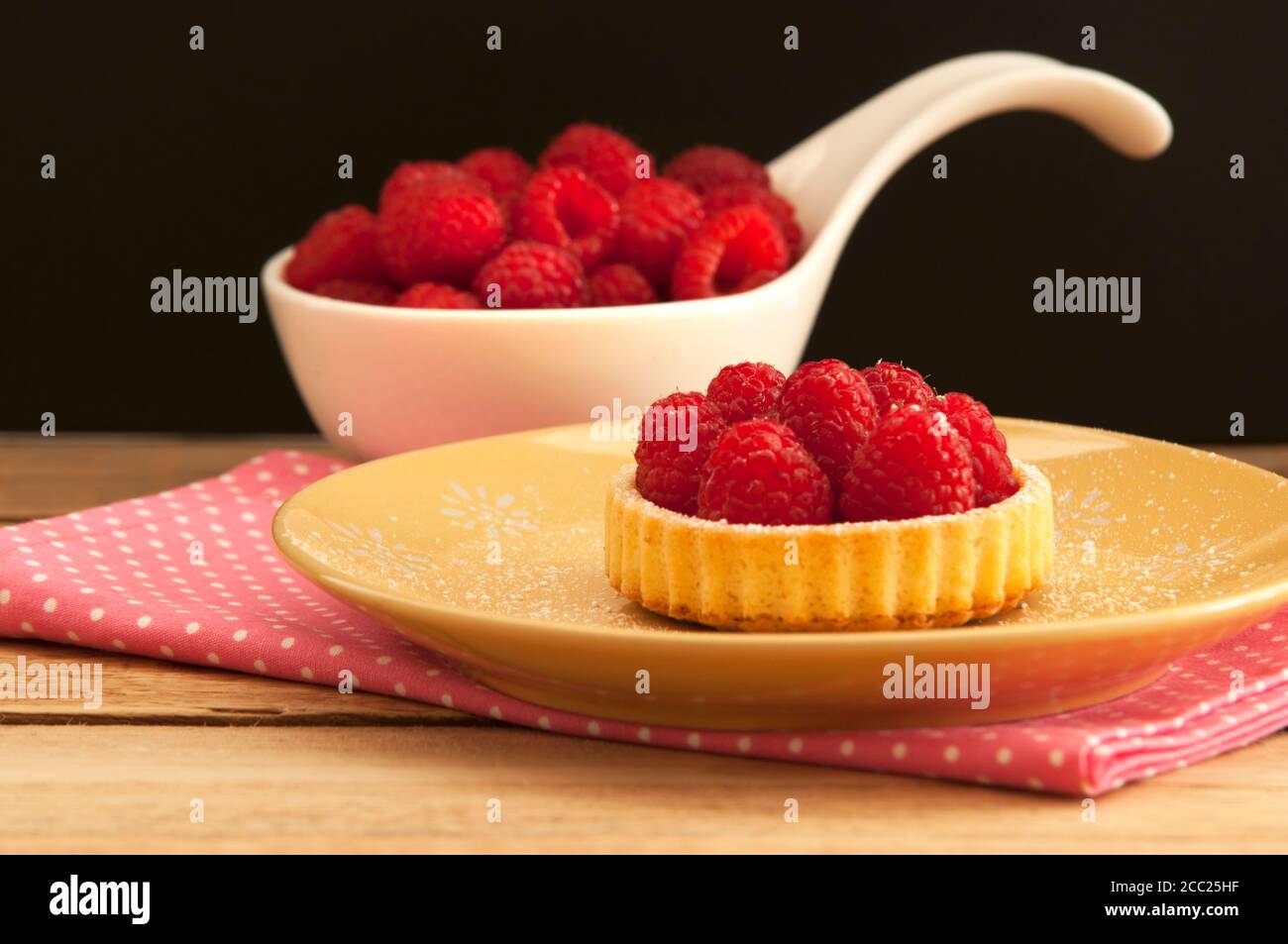 Cucchiaio di lamponi con tartlet e tovagliolo sulla tavola di legno, close up Foto Stock