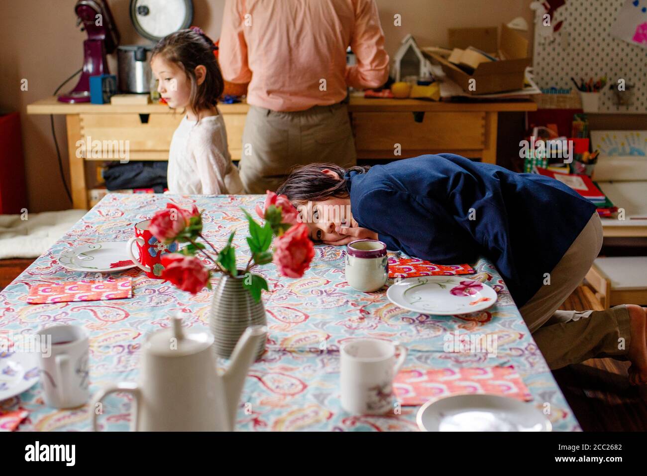 Un ragazzo in tuta si stende su un tavolo per il tè, famiglia in background Foto Stock