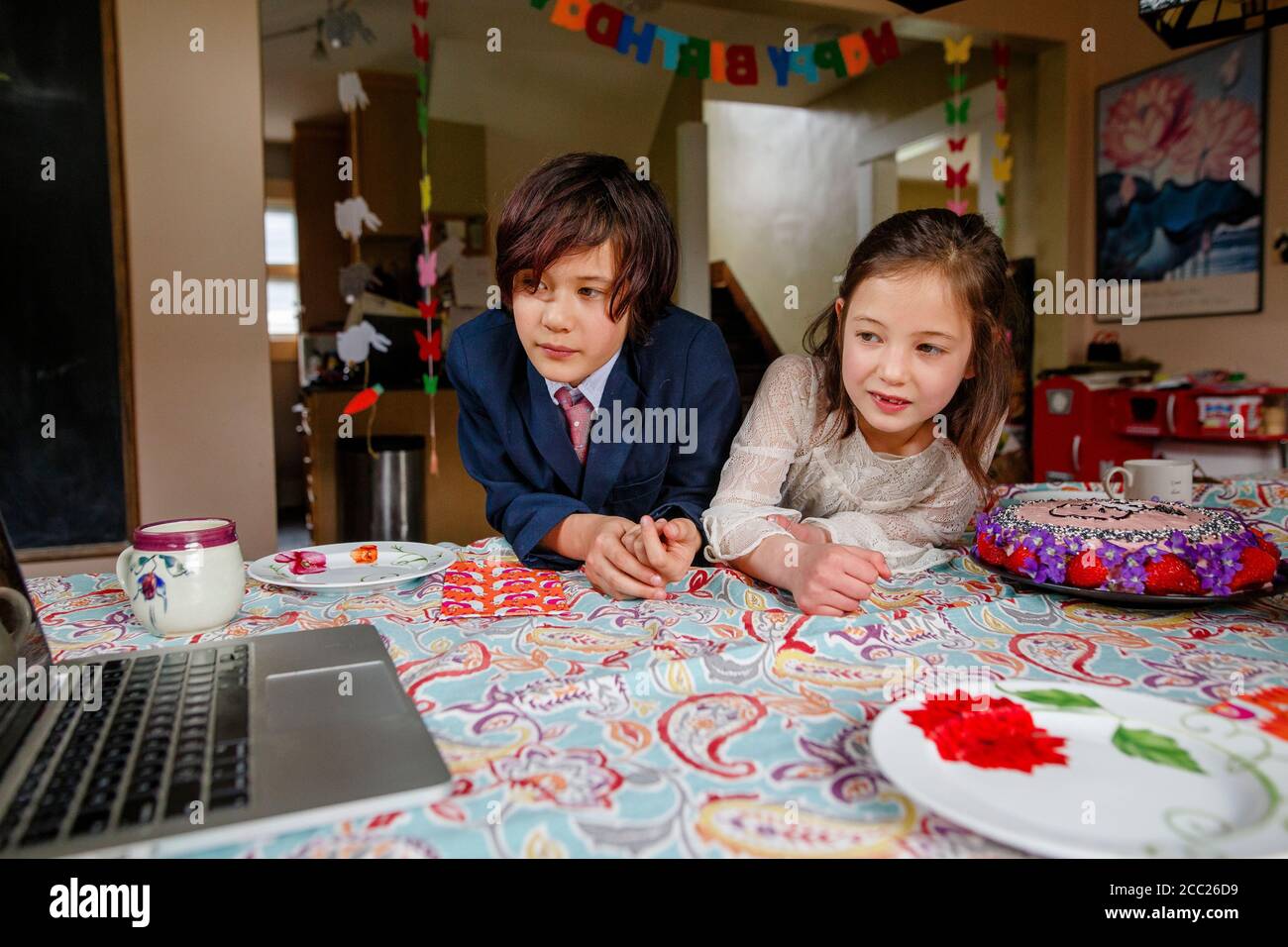 Un ragazzo e una ragazza si siedono a tavola con una torta di compleanno guardare un computer Foto Stock