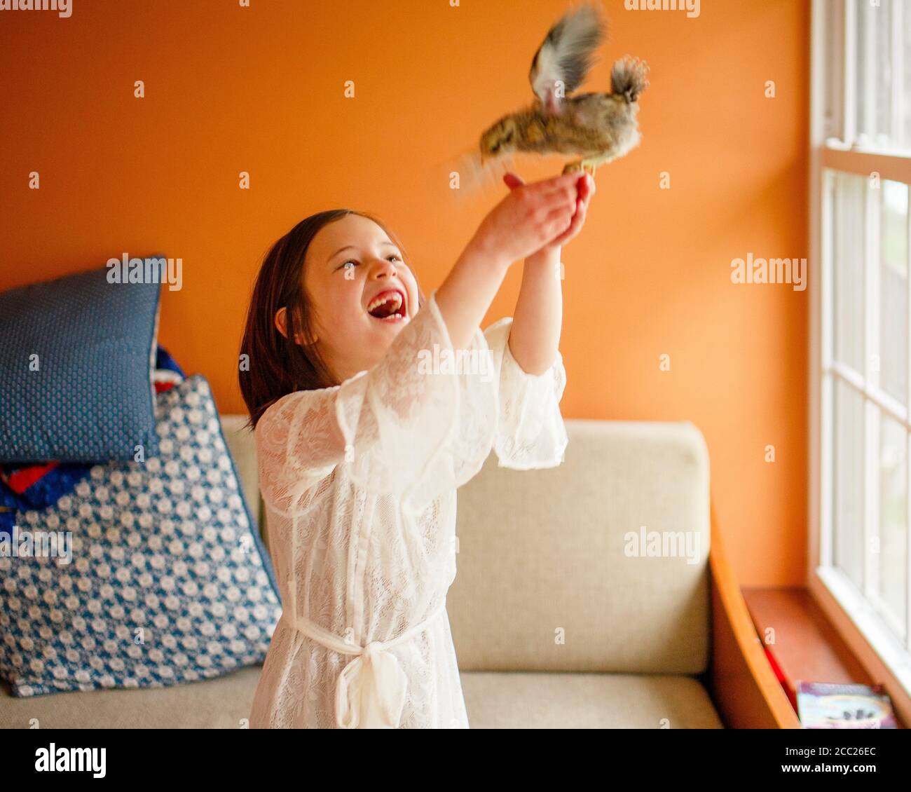 Un bambino ride con delizia tenendo un uccello flapping aloft nelle sue mani Foto Stock
