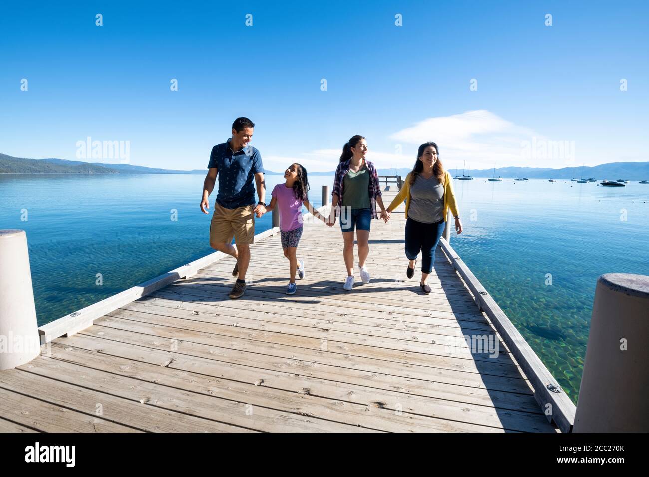 Una famiglia sorride e tiene le mani a piedi giù un molo in una giornata di sole a South Lake Tahoe, California. Foto Stock