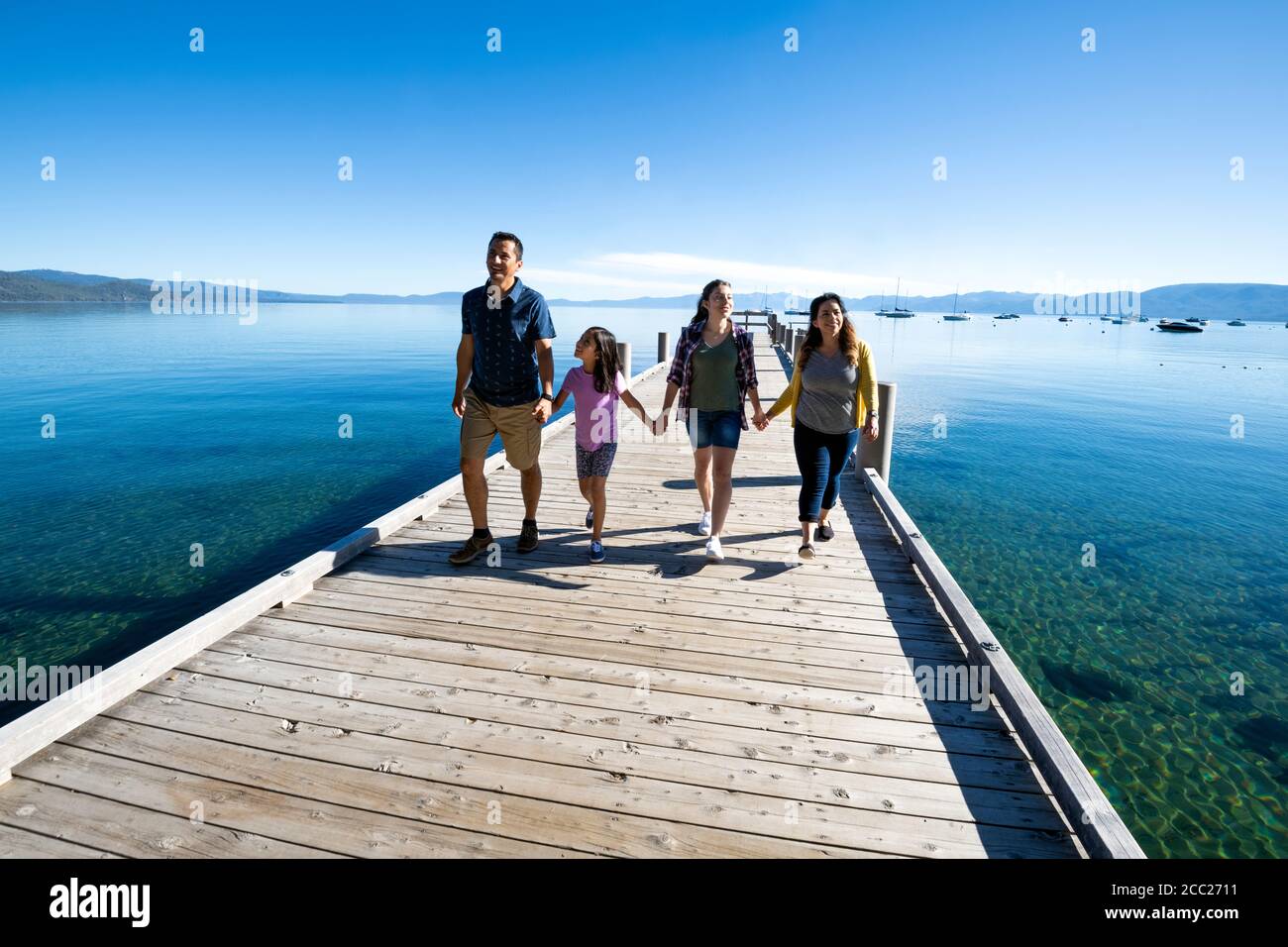 Una famiglia sorride e tiene le mani a piedi giù un molo in una giornata di sole a South Lake Tahoe, California. Foto Stock