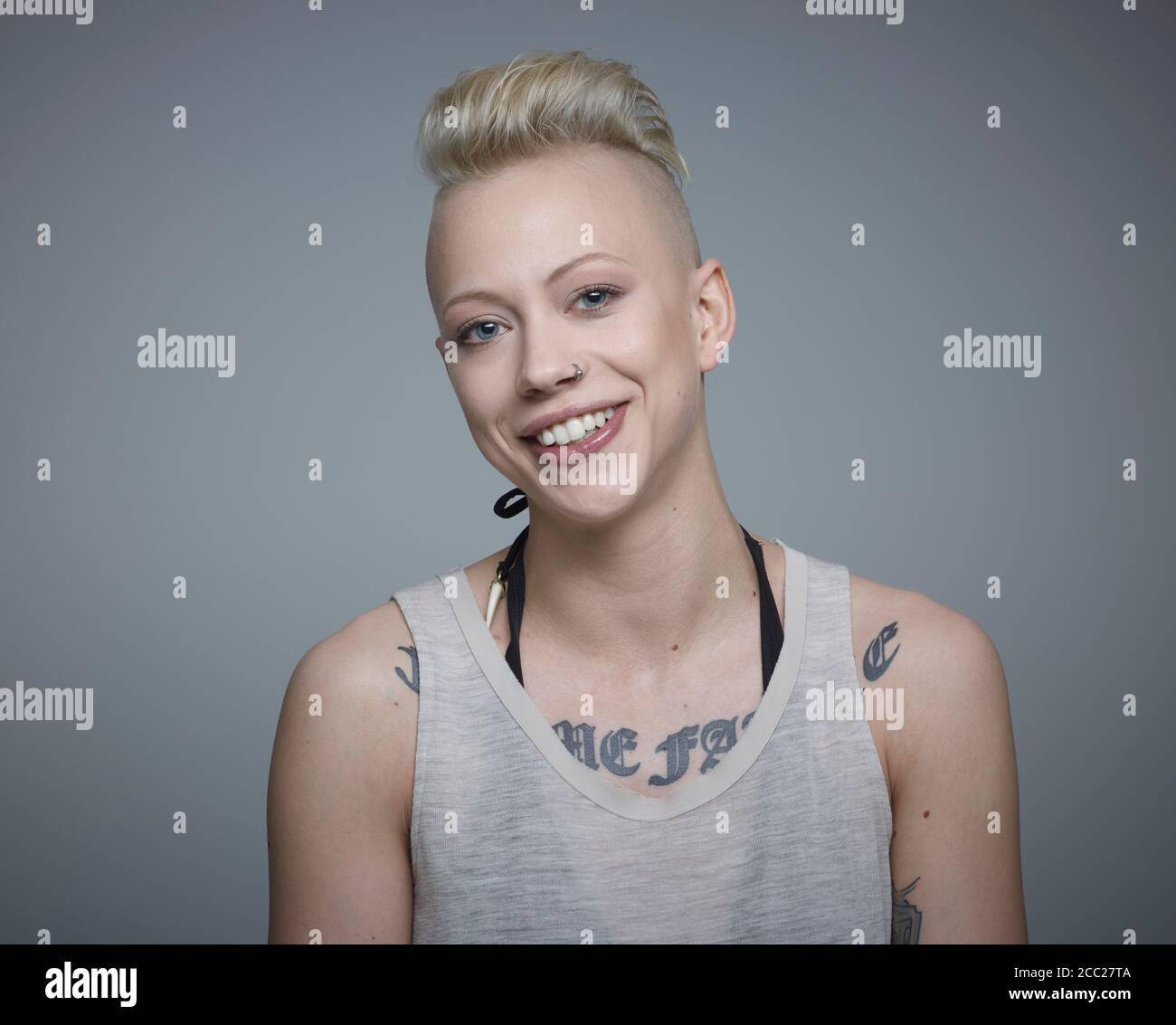 Ritratto di giovane donna con tatuaggi contro uno sfondo grigio, sorridente Foto Stock