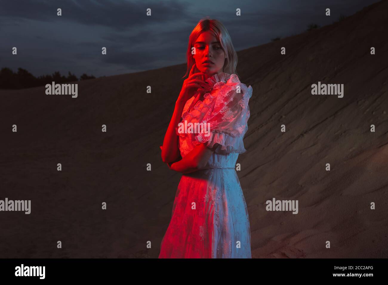 Donna in un lungo vestito in piedi vicino a una collina sabbiosa di sera Foto Stock