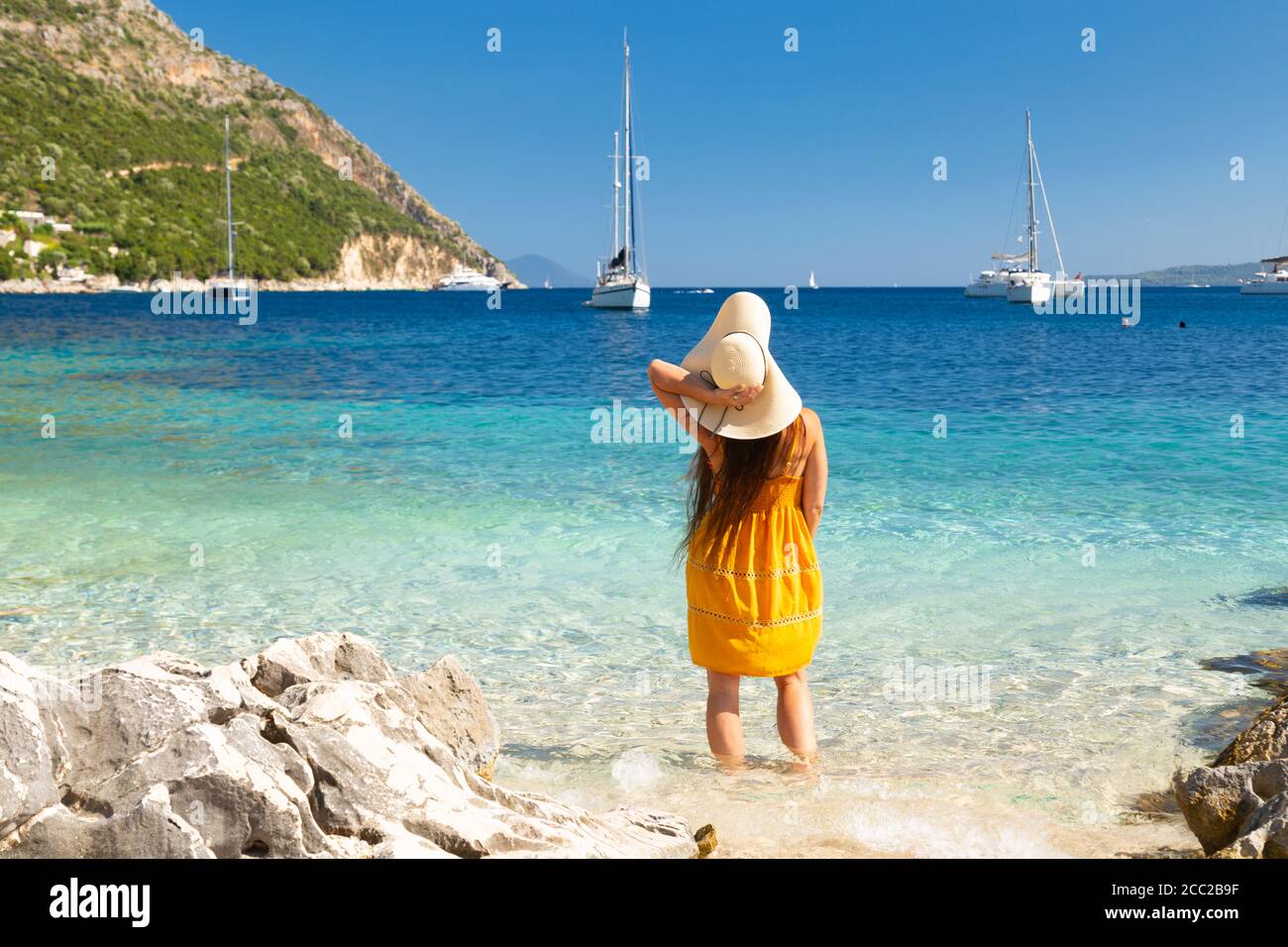 Una ragazza in abito giallo che guada in acque poco profonde e limpide a Lila Beach, vicino Mikros Gialos, Lefkada, Isole IONIE, Grecia Foto Stock