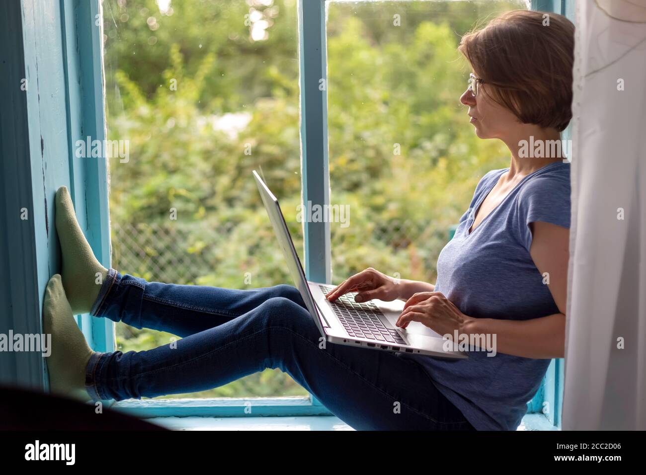 Donna freelance seduta su un davanzale che lavora su un notebook Foto Stock