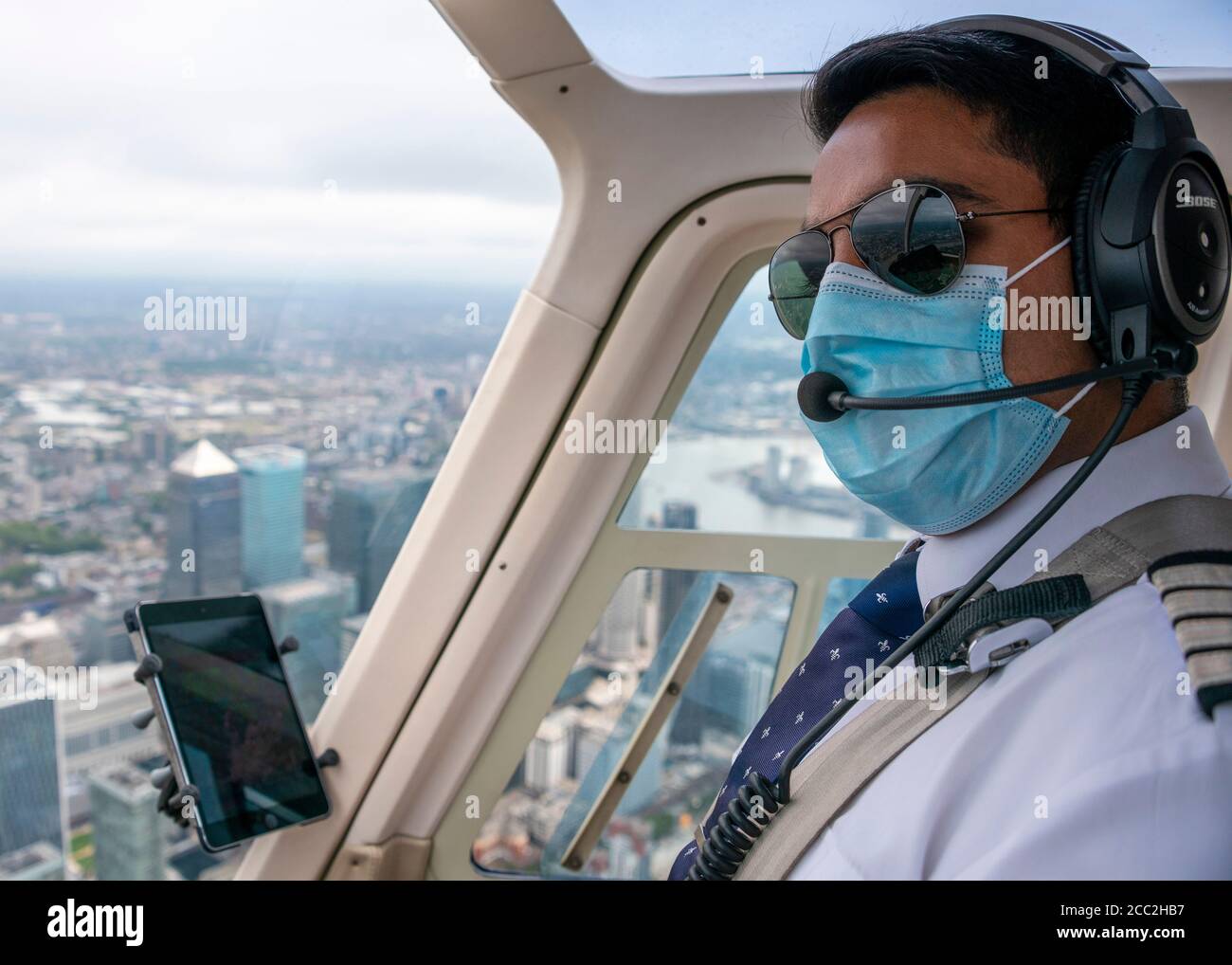 Ritratto orizzontale di un pilota che indossa una maschera che vola in elicottero sopra Canary Wharf a Londra. Foto Stock