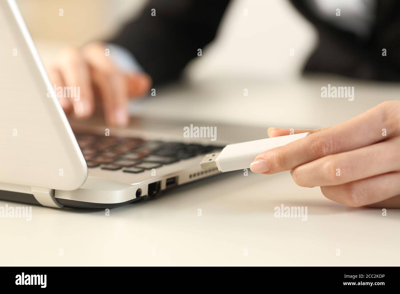 Primo piano di una donna esecutiva che collega le mani del pendrive sopra computer portatile seduto su una scrivania in ufficio Foto Stock