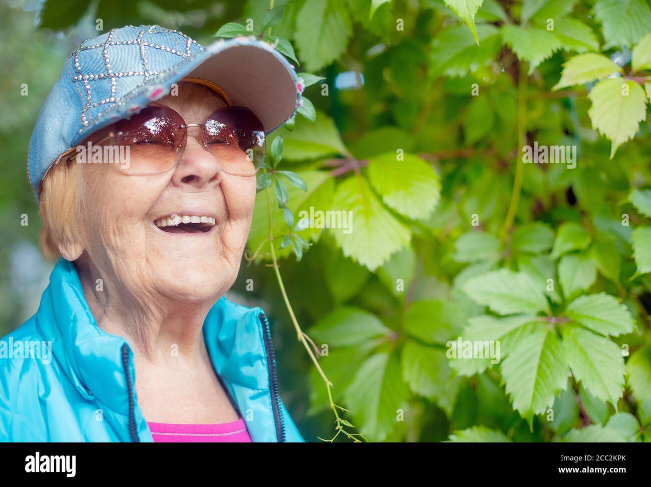 Nonna felice, alla moda di 90 anni con i capelli grigi, gli occhiali da sole e un sorriso nella natura in una giornata estiva di sole. Foto Stock