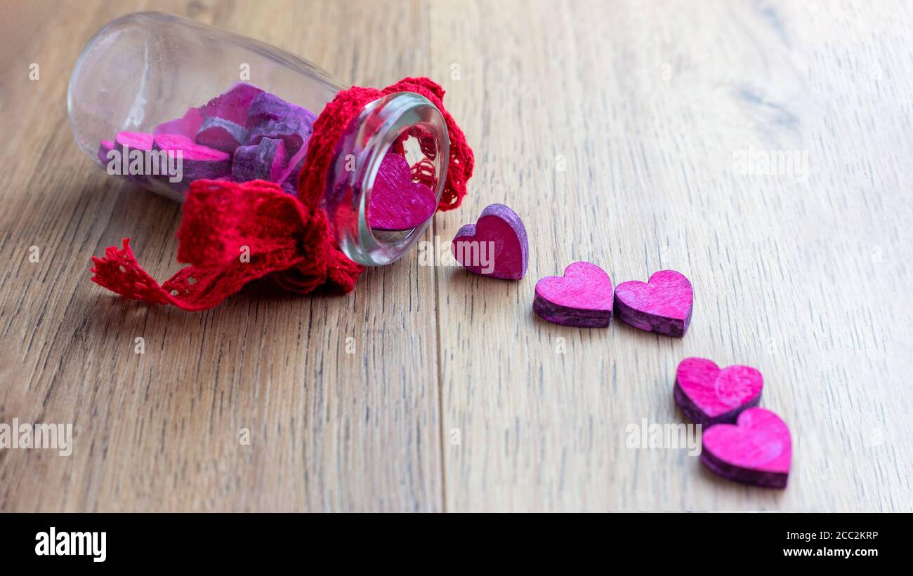 cuori rosa uscenti da bottiglia di vetro su tavolo di legno Foto Stock