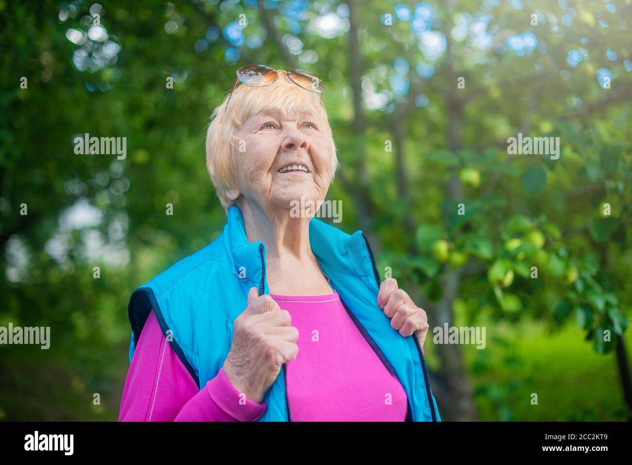 Nonna felice, alla moda di 90 anni con i capelli grigi, gli occhiali da sole e un sorriso nella natura in una giornata estiva di sole. Foto Stock