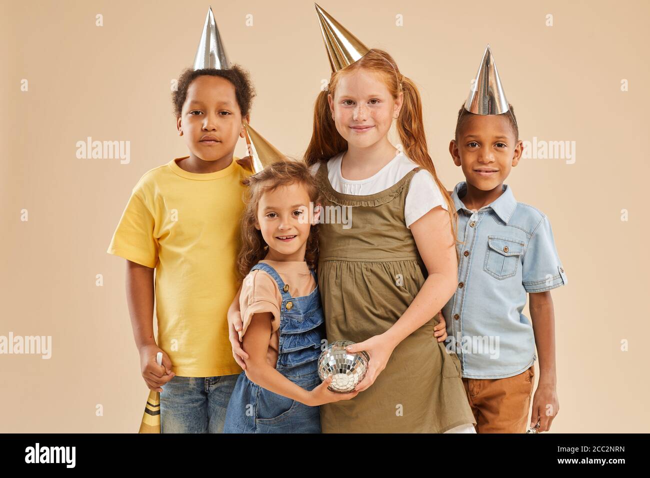 Ritratto in vita di diversi gruppi di bambini che indossano la festa cappelli che guardano la macchina fotografica mentre si levano in piedi contro lo sfondo normale dentro studio Foto Stock