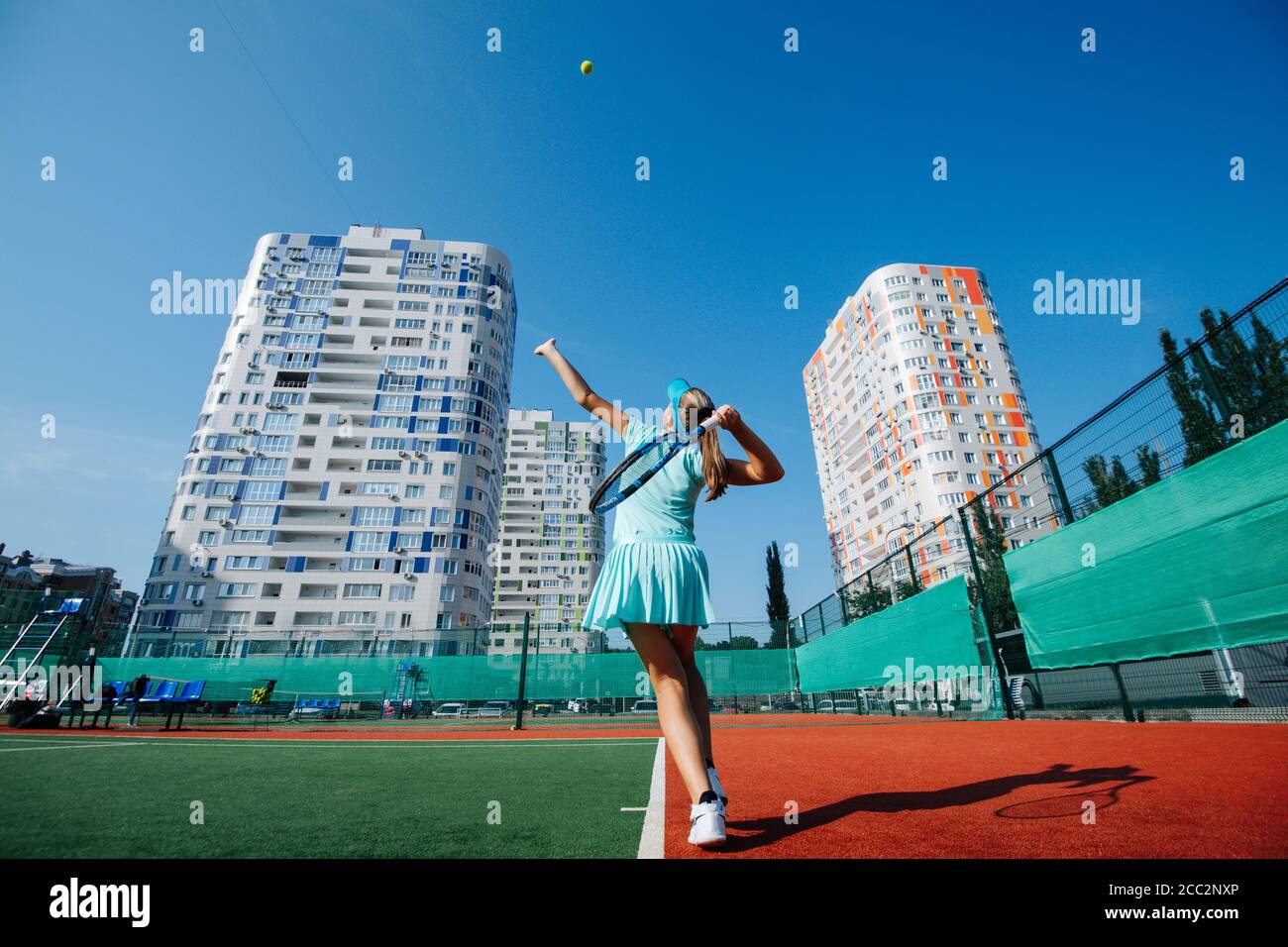 Adolescente ragazza formazione su un nuovo campo da tennis sotto a. bel cielo blu chiaro Foto Stock