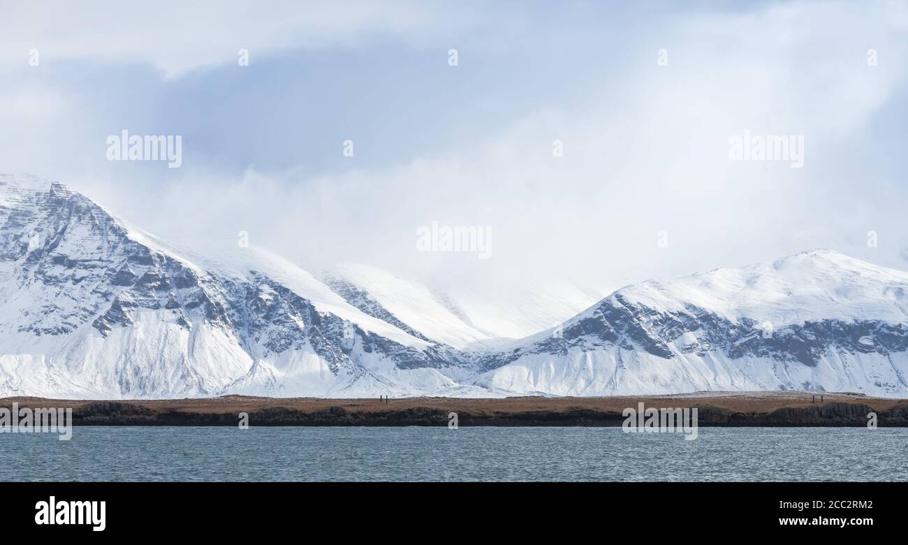 Paesaggio islandese con montagne costiere innevate sotto il cielo nuvoloso. Reykjavik, Islanda Foto Stock