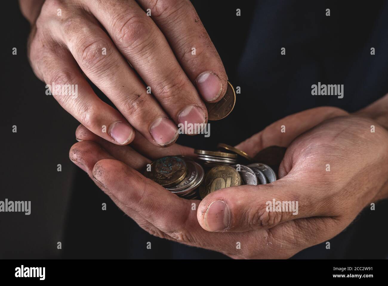 Le mani degli uomini tengono le monete ruble da vicino su uno sfondo scuro. Il concetto di povertà e miseria Foto Stock