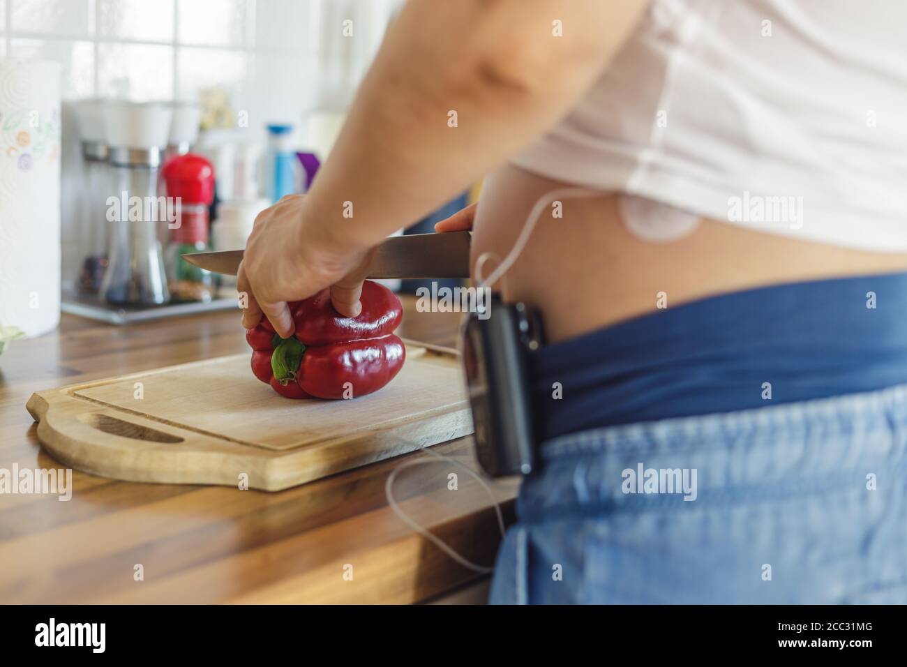 Donna incinta con pompa insulina sui suoi pantaloni e drenaggio montato sul ventre in cucina preparando cibo sano. Moderno trattamento del diabete. Foto Stock