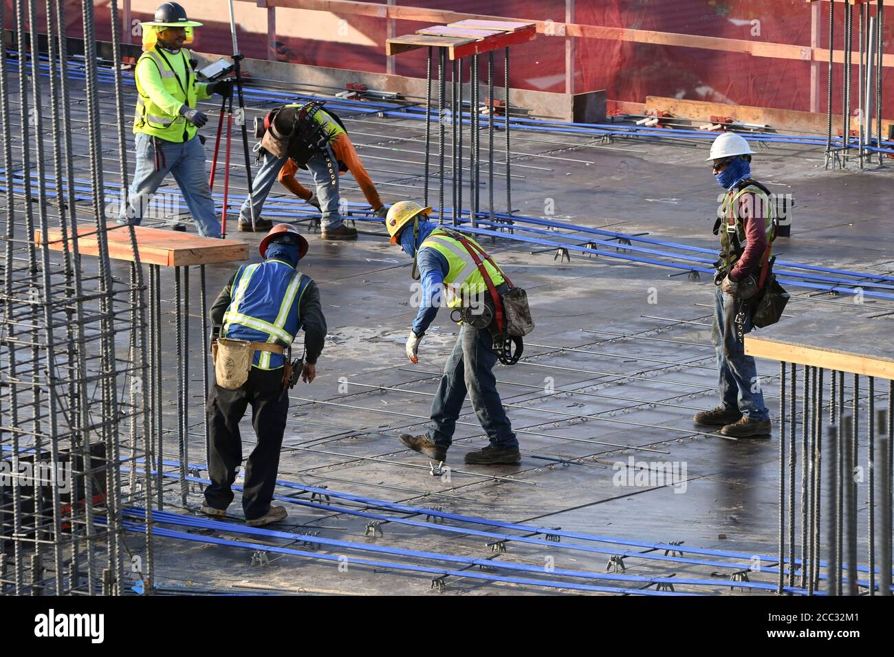 L'equipaggio di costruzione che indossa attrezzatura di sicurezza completa e rivestimenti del viso lavora su forme di costruzione per colonne di cemento per garage di alta torre che sale nel quartiere di Rainey Street vicino al centro di Austin Texas. Foto Stock