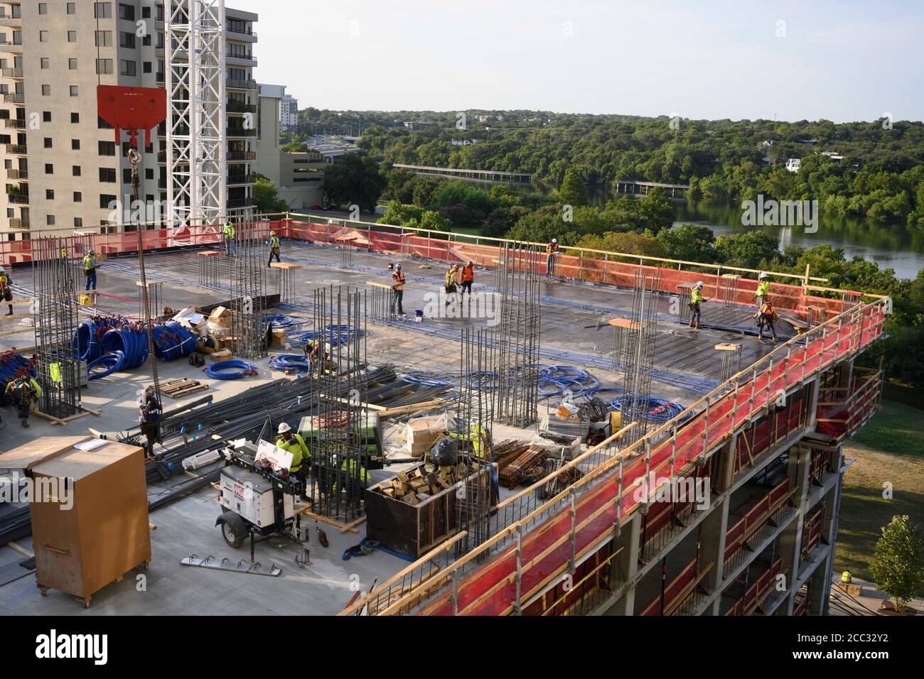 L'equipaggio di costruzione che indossa attrezzatura di sicurezza completa e rivestimenti del viso lavora su forme di costruzione per colonne di cemento per garage di alta torre che sale nel quartiere di Rainey Street vicino al centro di Austin Texas. Foto Stock