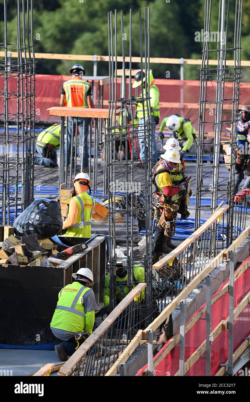 L'equipaggio di costruzione che indossa attrezzatura di sicurezza completa e rivestimenti del viso lavora su forme di costruzione per colonne di cemento per garage di alta torre che sale nel quartiere di Rainey Street vicino al centro di Austin Texas. Foto Stock