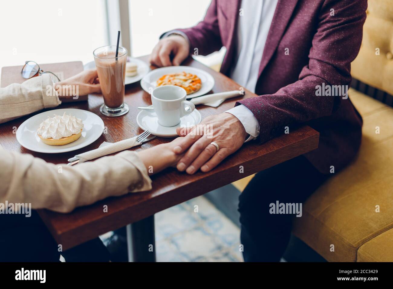 uomo anziano che tiene la mano della moglie mentre si siede nel caffè. uomo che sostiene la sua donna in una situazione difficile, coppia che supera i problemi della famiglia Foto Stock