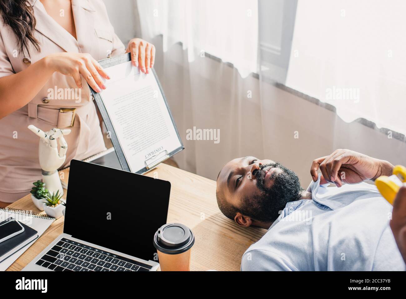 Fuoco selettivo di businesswoman che soffia con gli appunti su amerian africano collega che soffre di calore in ufficio Foto Stock