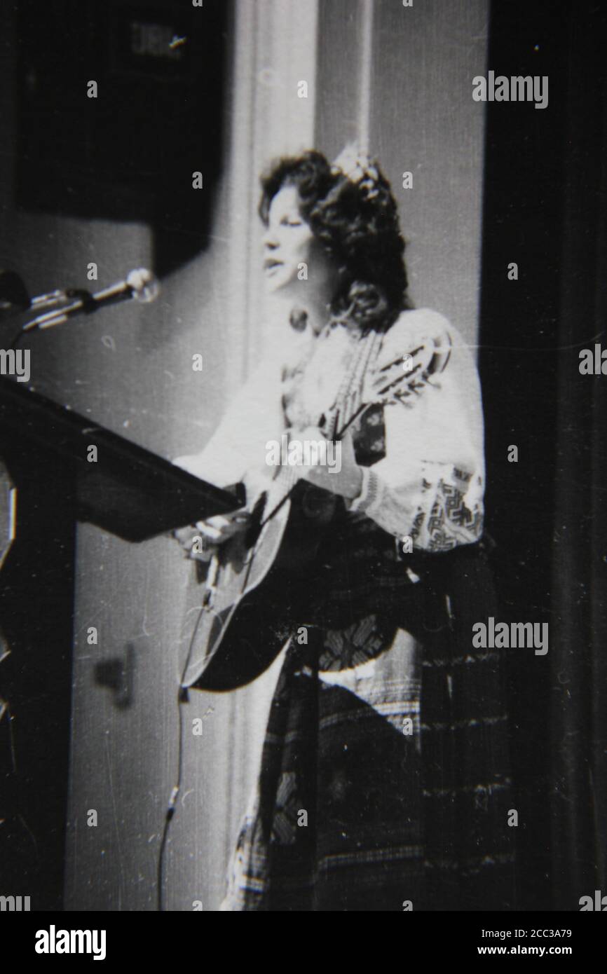 Bella fotografia in bianco e nero d'epoca degli anni '70 di una donna etnica dell'Europa orientale che suona la chitarra sul palco indossando abiti etnici. Foto Stock