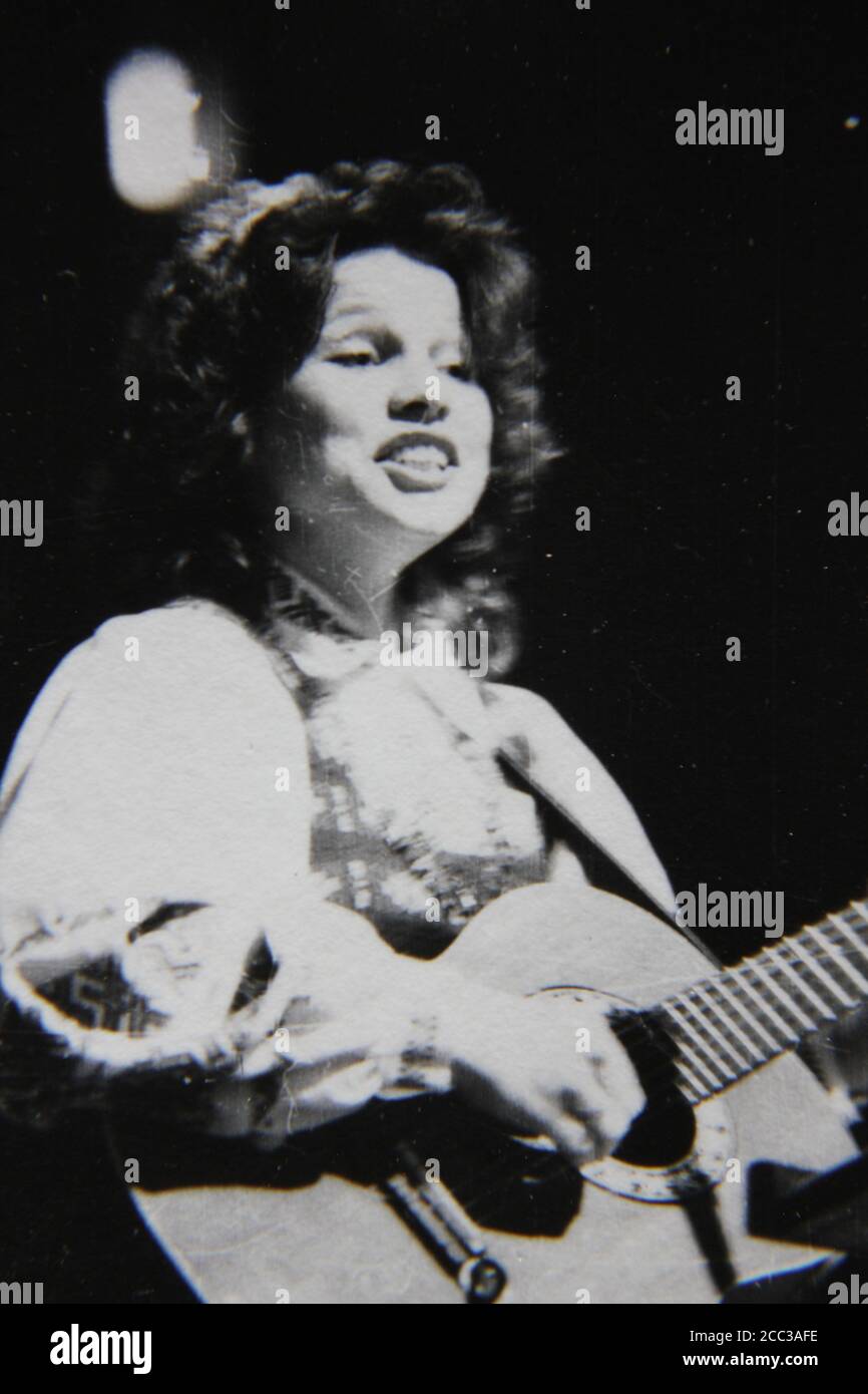 Bella fotografia in bianco e nero d'epoca degli anni '70 di una donna etnica dell'Europa orientale che suona la chitarra sul palco indossando abiti etnici. Foto Stock