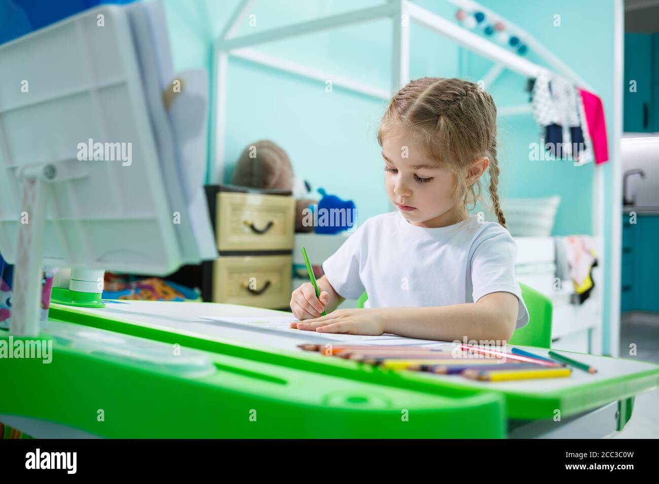 Ritratto di una bambina carina che guarda la macchina fotografica e sorride mentre disegnano le immagini o fanno i compiti, seduto ad un tavolo nell'interno domestico Foto Stock