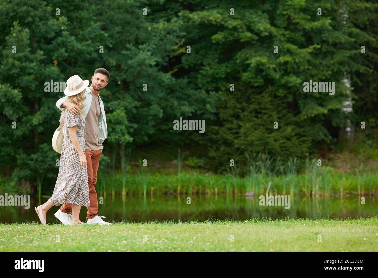 Vista laterale ritratto di una romantica coppia di adulti che si abbraccia mentre si cammina lungo il fiume in rustico paesaggio di campagna, copia spazio Foto Stock
