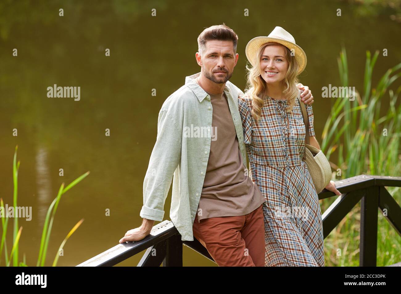 Ritratto di una romantica coppia di adulti guardando la macchina fotografica mentre ci si trova vicino al lago all'aperto in un paesaggio rustico, spazio copia Foto Stock