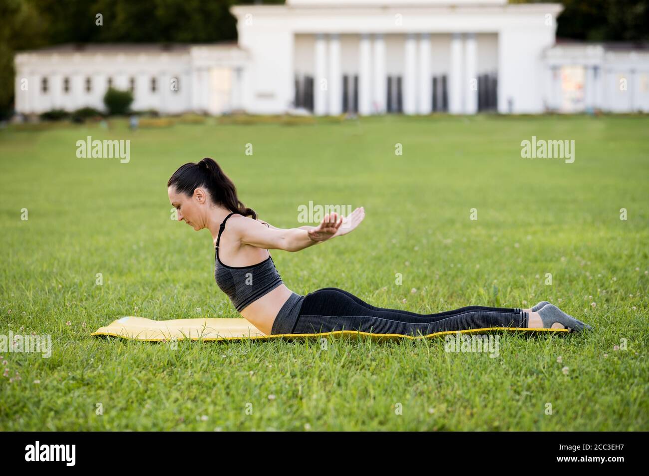 Bella giovane donna sdraiata su un materasso giallo, posa mentre indossa un vestito sportivo stretto nel parco facendo pilates o yoga, esperto di immersione in cigno exercis Foto Stock