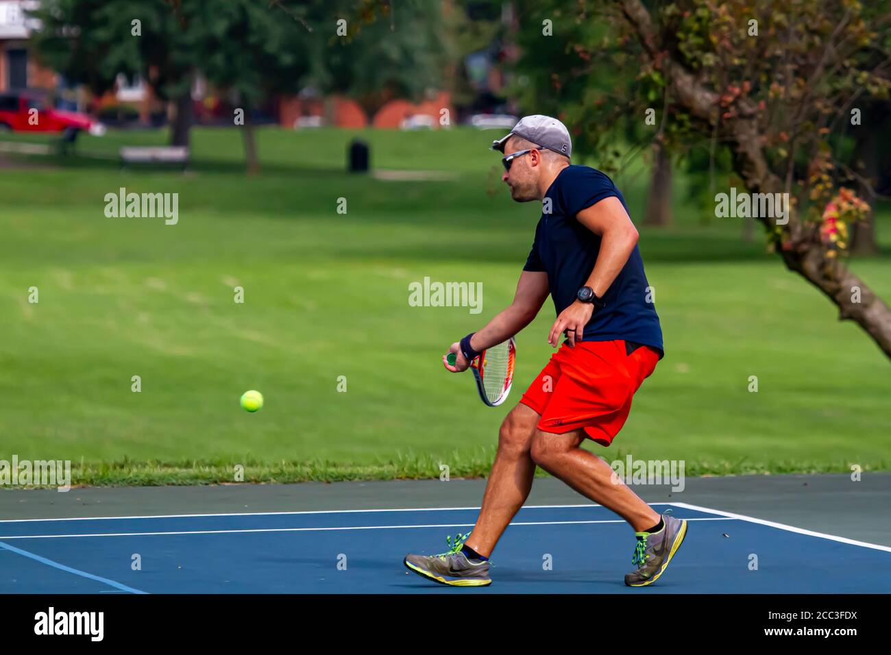 Maryland, USA 08/14/2020: Un uomo caucasico atletico che indossa t-shirt blu e short rosso gioca a tennis in un campo locale a Baker Park, Frederick. H Foto Stock