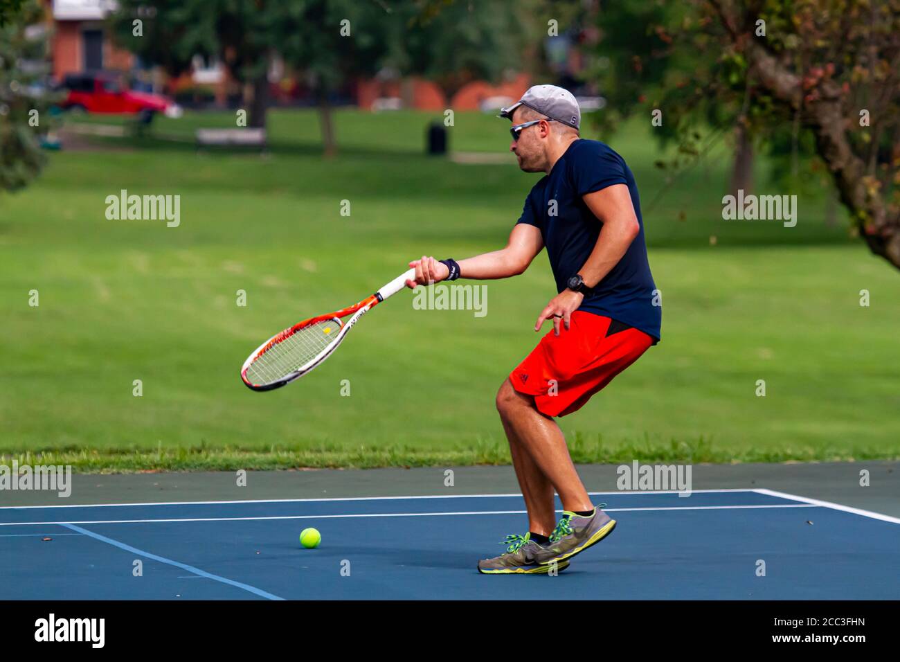 Maryland, USA 08/14/2020: Un uomo caucasico atletico che indossa t-shirt blu e short rosso gioca a tennis in un campo locale a Baker Park, Frederick. H Foto Stock