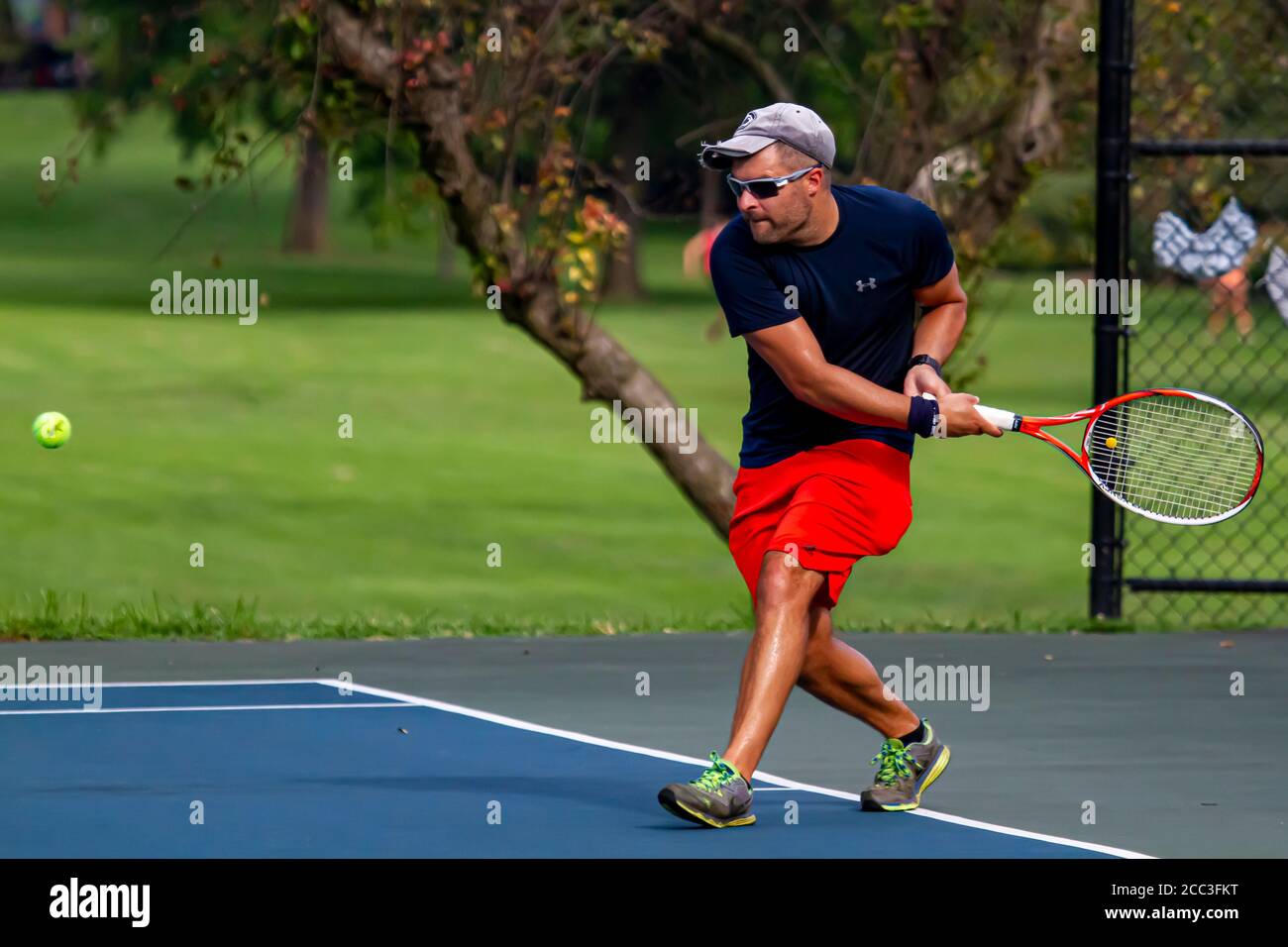Maryland, USA 08/14/2020: Un uomo caucasico atletico che indossa t-shirt blu e short rosso gioca a tennis in un campo locale a Baker Park, Frederick. H Foto Stock