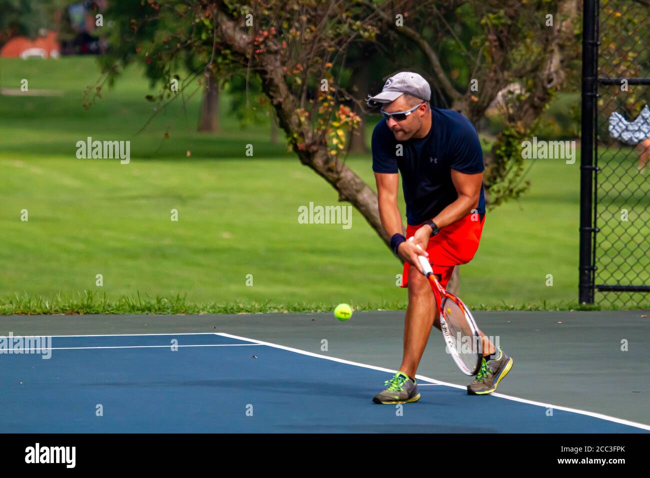 Maryland, USA 08/14/2020: Un uomo caucasico atletico che indossa t-shirt blu e short rosso gioca a tennis in un campo locale a Baker Park, Frederick. H Foto Stock