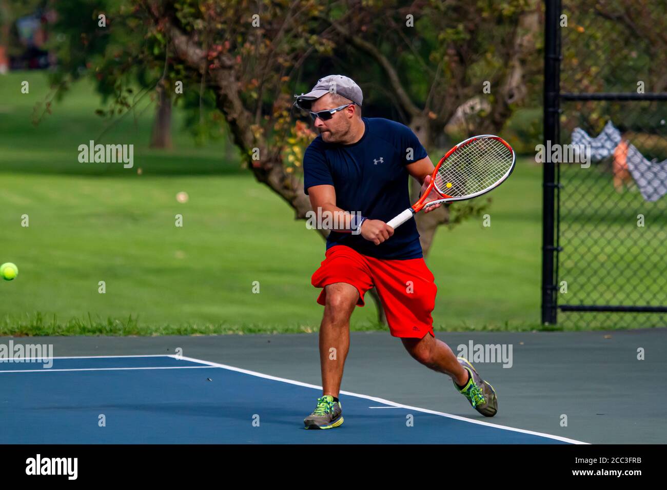 Maryland, USA 08/14/2020: Un uomo caucasico atletico che indossa t-shirt blu e short rosso gioca a tennis in un campo locale a Baker Park, Frederick. H Foto Stock