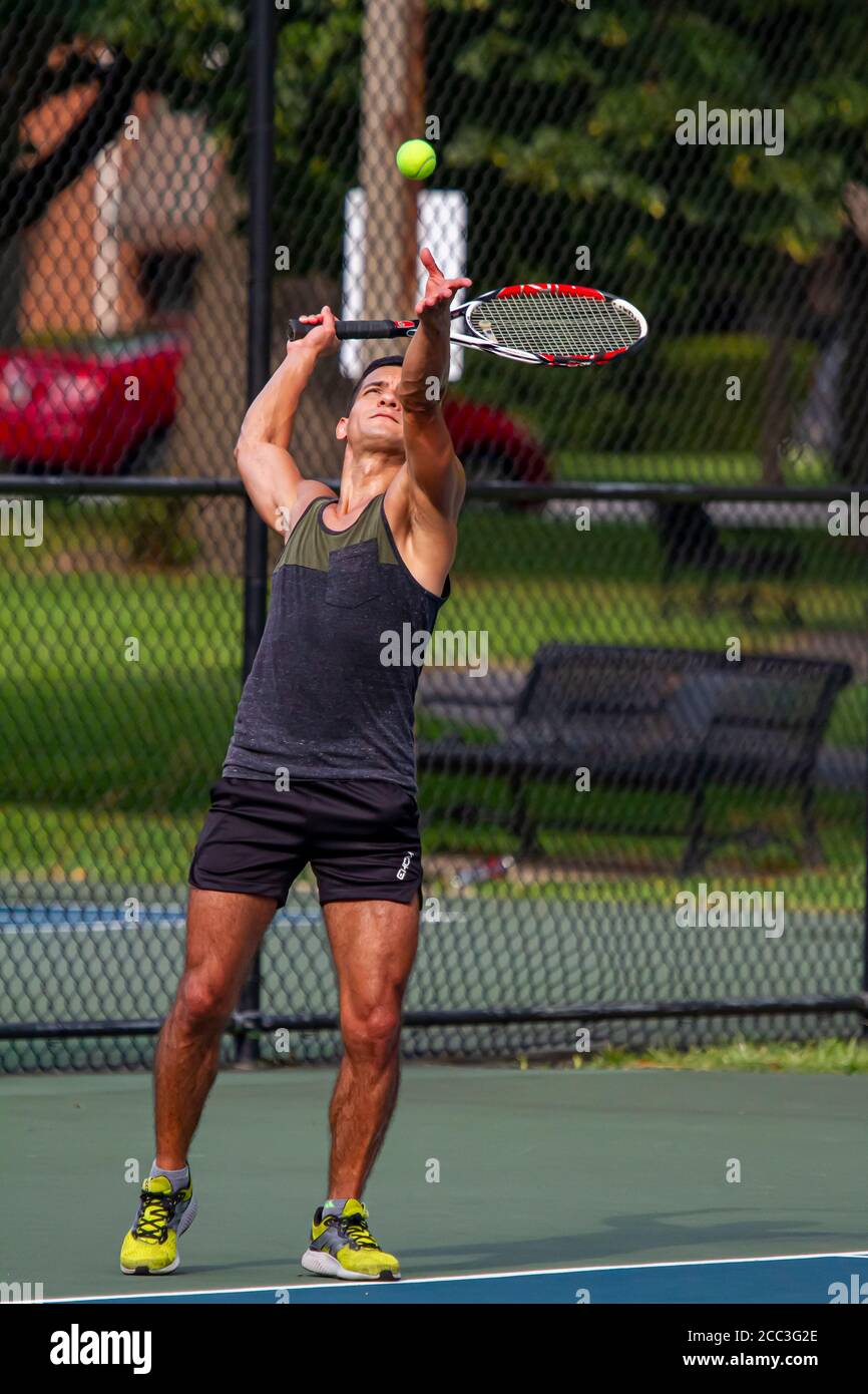 MD, USA 08/14/2020: Un atletico ispanico che indossa una camicia e un pantaloncini senza maniche sudati sta prendendo un servizio durante una partita di tennis in un campo locale a Ba Foto Stock