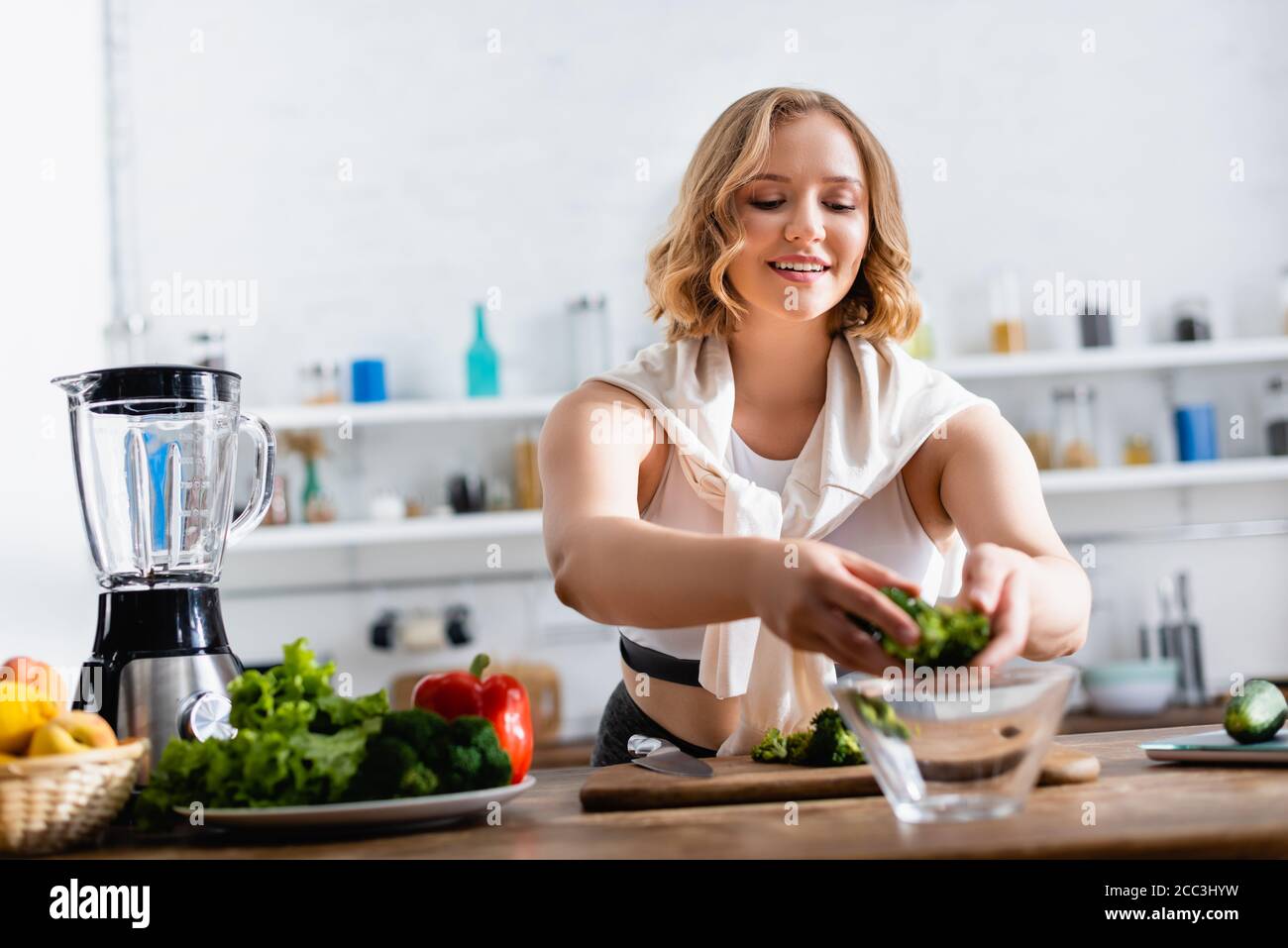 fuoco selettivo della giovane donna che mette i broccoli nella ciotola vicino verdure Foto Stock