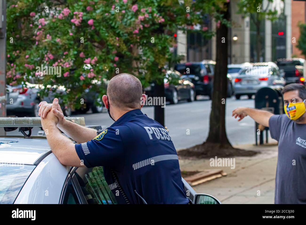 Frederick, MD, USA 08/14/2020: Un giovane poliziotto maschio caucasico che indossa una maschera sta rispondendo ad una domanda posta da una persona che indossa anche Foto Stock