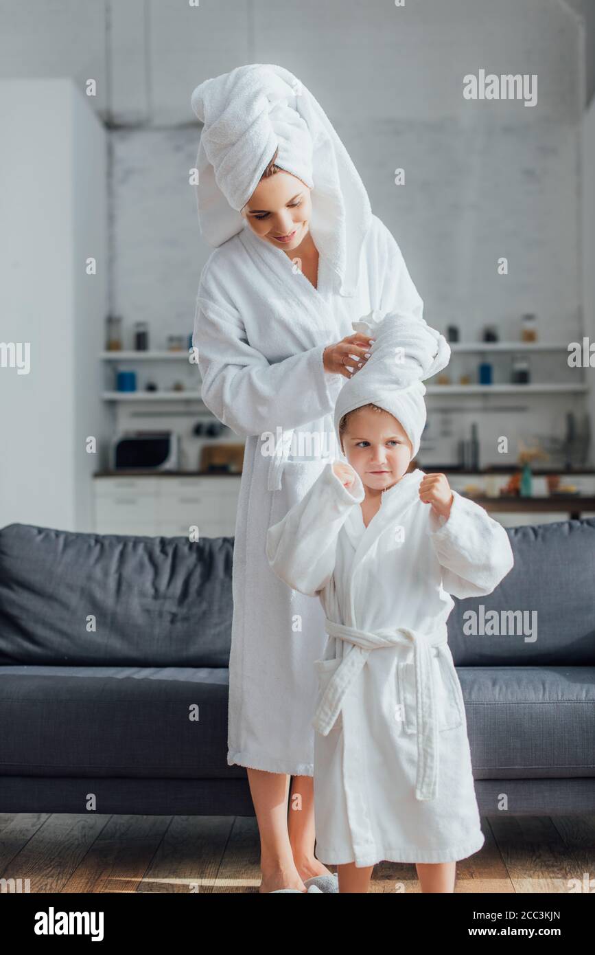 giovane donna che fissa asciugamano sulla testa della figlia in bianco  accappatoio in spugna mentre ci si trova vicino al divano Foto stock - Alamy