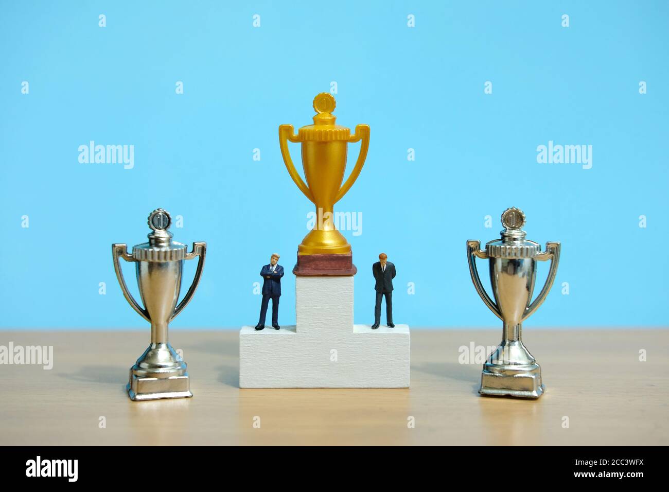 Concetto di business in miniatura - uomo d'affari in piedi sul podio bianco vincitore con trofeo d'oro e d'argento Foto Stock