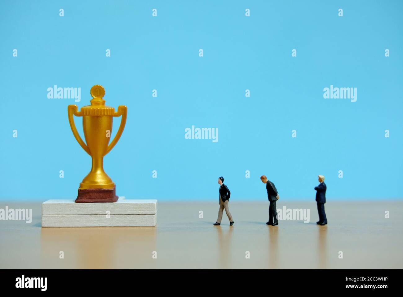 Concetto di business in miniatura - gruppo di uomini d'affari che si allineano dietro il trofeo d'oro Foto Stock