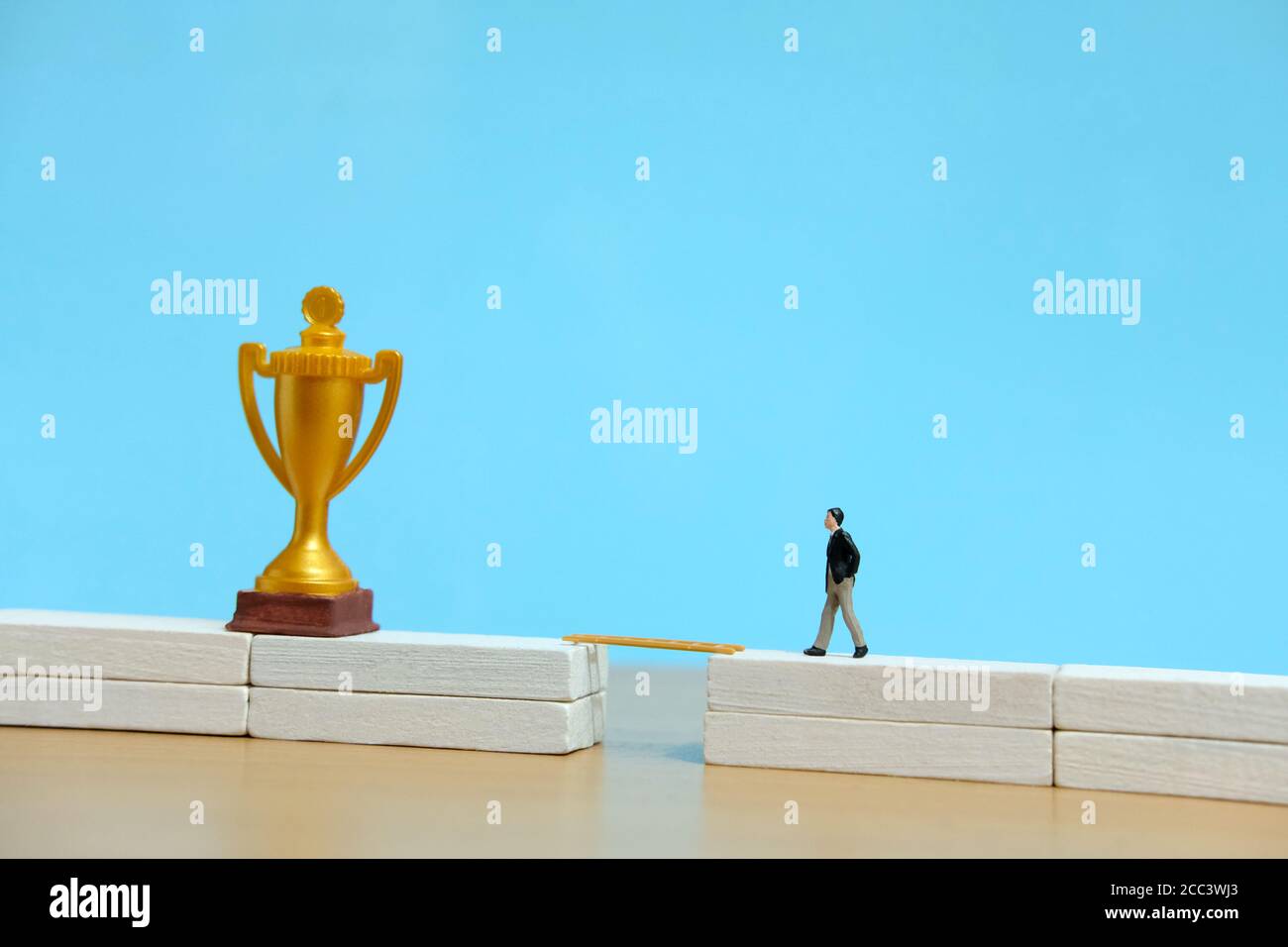 Concetto di business in miniatura - uomo d'affari che cammina verso il trofeo d'oro sopra ponte bianco Foto Stock